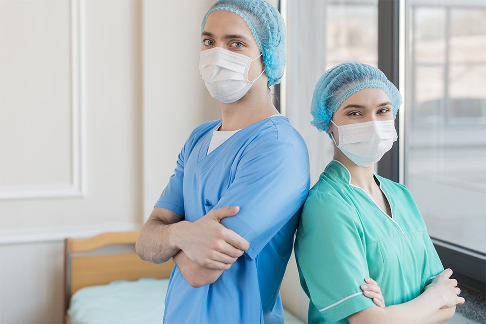 Two nurses stand back to back with masks on.